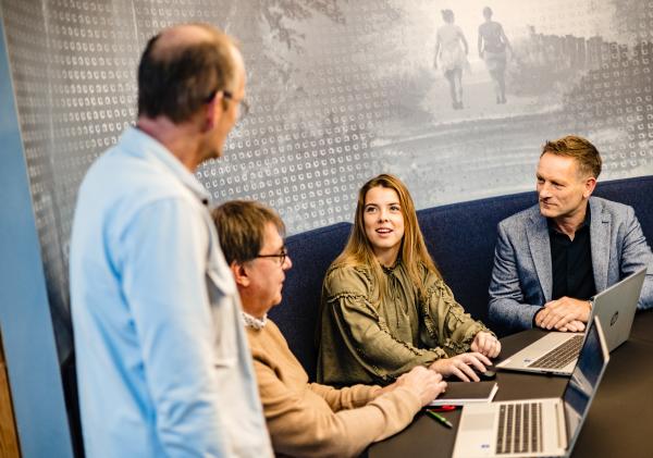 Vier collega's zittend op een bank met laptops op tafel