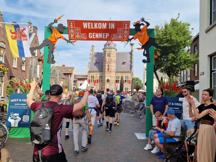 Wandelaars lopen de banner Welkom in Gennep onderdoor